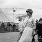 Dagenham Town Show 1965, showing a group of people including a woman in white walking past the marquee, 1965