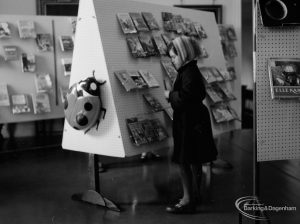 Barking Libraries exhibition at Valence House, Dagenham for National Book Week, showing young girl in a scarf examining a book in the ‘Primary’ area, 1966