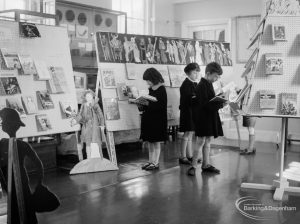Barking Libraries exhibition at Valence House, Dagenham for National Book Week, showing three children examining books standing by a cardboard cut-out of Long John Silver, 1966