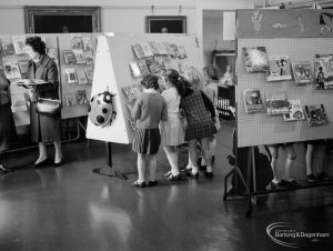 Barking Libraries exhibition at Valence House, Dagenham for National Book Week, showing a mother on one side of a display stand and four children examining books, 1966