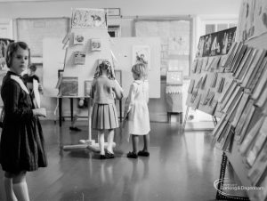 Barking Libraries exhibition at Valence House, Dagenham for National Book Week, showing three girls standing at the central display on the east end of the room, 1966
