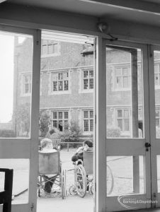 Training Centre at Eastbury House, Barking, showing view from inside Solarium showing two wheelchair users in grounds, with Eastbury House beyond, 1966