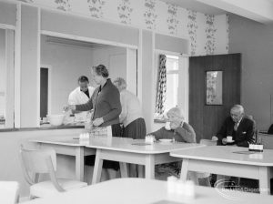 Mayesbrook, Bevan Avenue, Barking, showing four elderly ladies in the dining room; two sitting at the tables and two receiving food, and the chef in the background, 1966