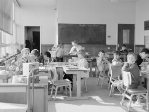 Faircross Special School, Hulse Avenue, Barking, showing classroom with sunlit desks and children, and with blackboard in background, 1967