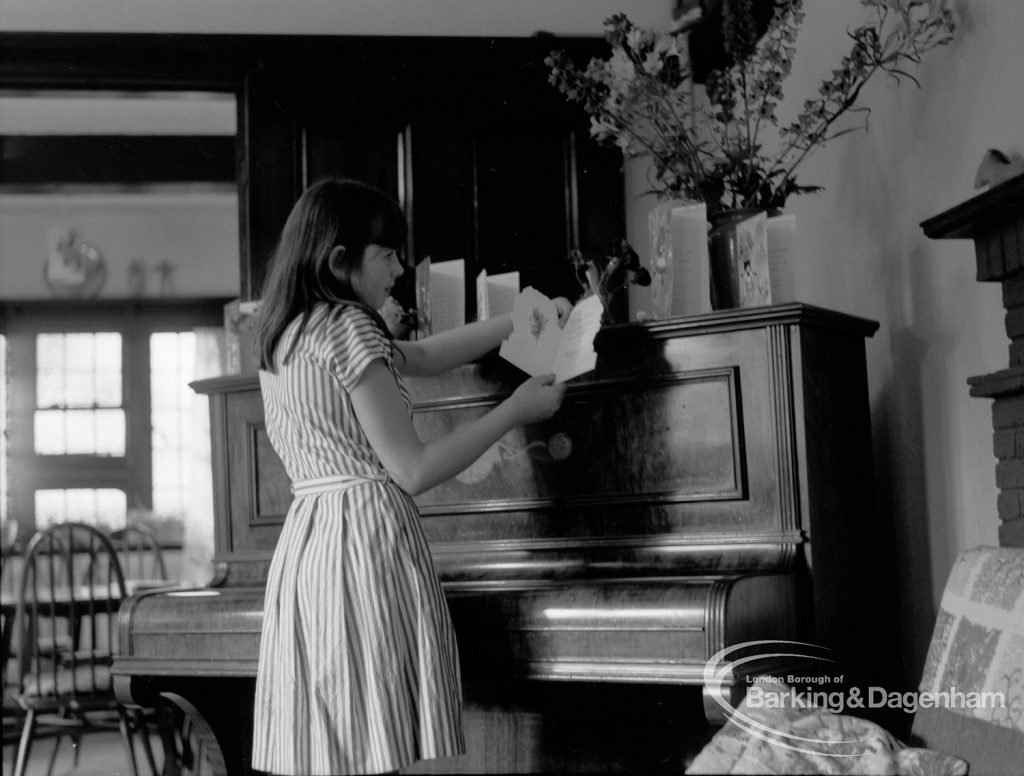 Child Welfare at Tudor House, 212 Becontree Avenue, Dagenham, showing girl standing at piano, looking at her birthday cards, 1968