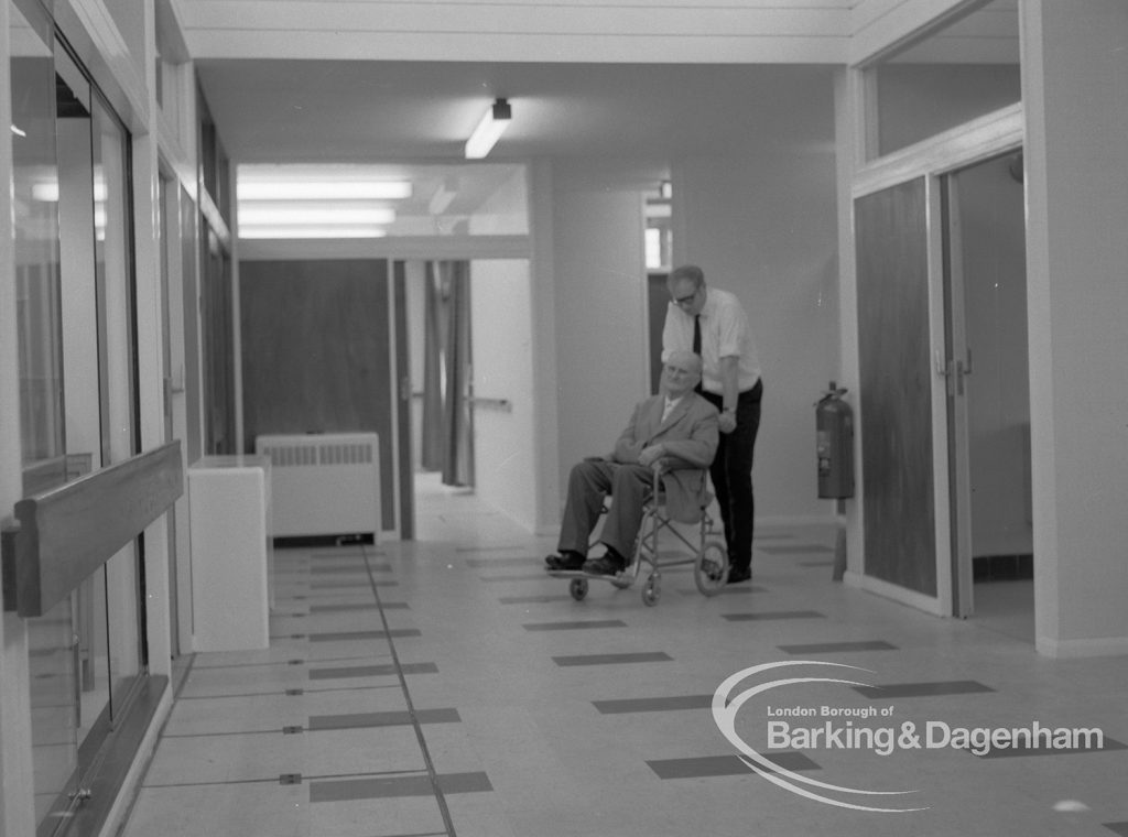 Welfare, showing Leys Avenue Occupational Centre for the Physically Handicapped, Dagenham, with member of staff pushing wheelchair user in hall, 1968