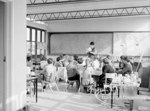 New William Bellamy Primary School, Becontree Heath, showing classroom on west side with children seated around tables and listening to teacher, 1970