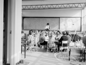 New William Bellamy Primary School, Becontree Heath, showing classroom at east, with class of children seated around tables and female teacher, 1970