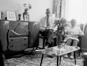 Housing at Grand Courts, Valence Wood Road, Dagenham, showing couple seated in lounge at flat and large sideboard to left, 1970