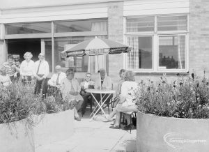 London Borough of Barking Welfare Department, Leys Training Centre Dagenham, showing groups of people standing and sitting on patio amongst flower-filled tubs, 1971