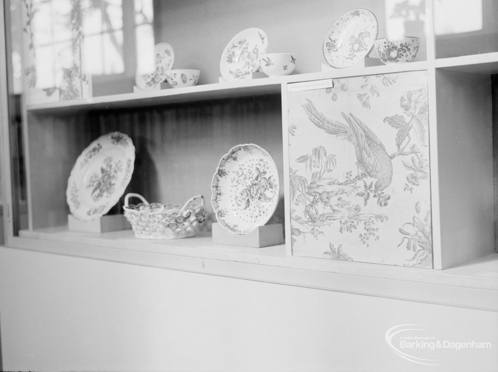 Victoria and Albert exhibition of English transfer-printed pottery and porcelain at Rectory Library, Dagenham, showing plates, cups and basket in cabinet, 1971