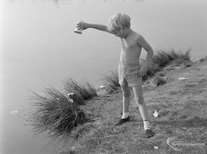 Barking Carnival 1971 from Mayesbrook Park, showing a young boy emptying a cup at the side of the lake, 1971