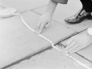 Highways, showing official measuring depth of defective paving in Heathway, Dagenham at junction with Pettits Road, 1971
