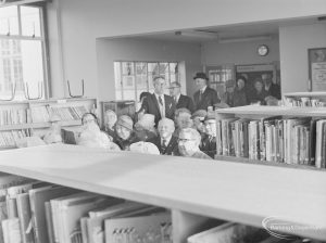 Standing and seated group of men and women waiting to apply for their bus permits in Children’s Library at Rectory Library, Dagenham, 1972