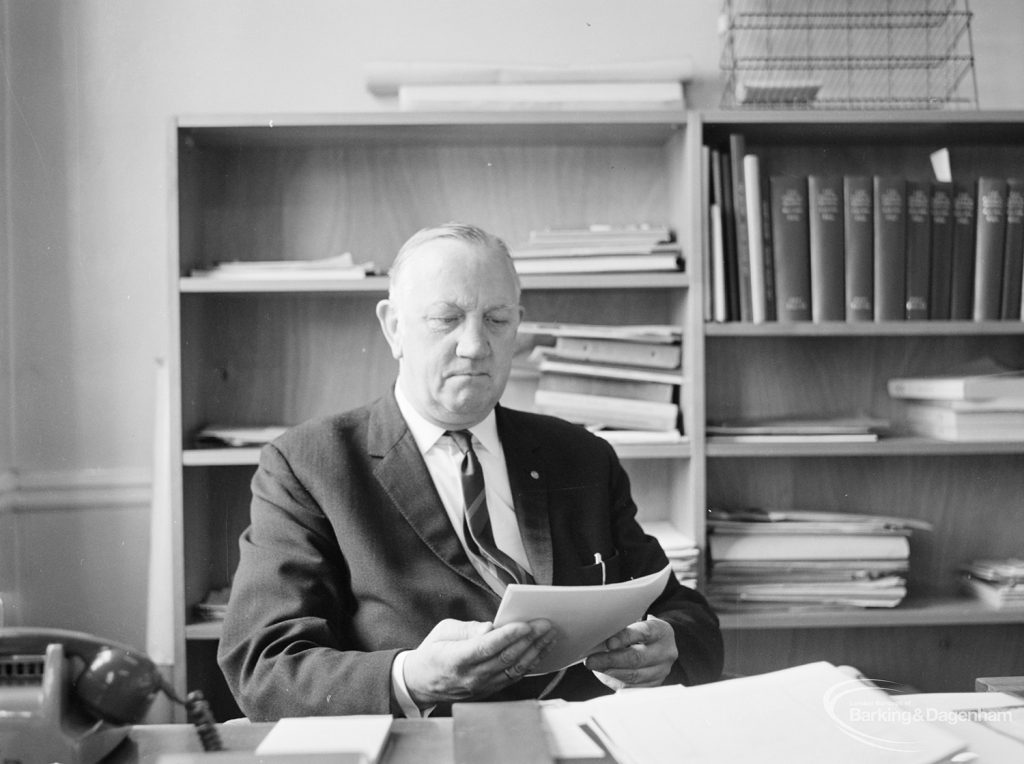 London Borough of Barking Borough Librarian Mr E W McManus FLA at his desk, looking down at a paper, 1972