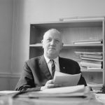 London Borough of Barking Borough Librarian Mr E W McManus FLA at his desk, looking up at photographer, 1972