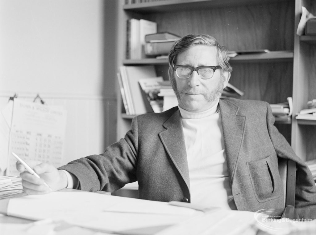 London Borough of Barking Deputy Borough Librarian Mr L Cannon FLA, sitting at his desk with arms extended, 1972