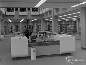 New Barking Central Library, Axe Street, Barking, showing bookcases and front view of staffed counter in Lending section, 1974
