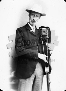 Man in hat holding camera on folded tripod,