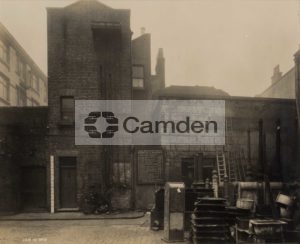 View of the entry into Green Dragon Yard, the works depot behind Holborn Town Hall. Various ladders, manhole covers and street bins are seen piled up to the right of the picture