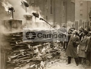 General Hamilton lights bonfire during ceremonial burning of models of vermin to mark start of building St Christopher's Flats
