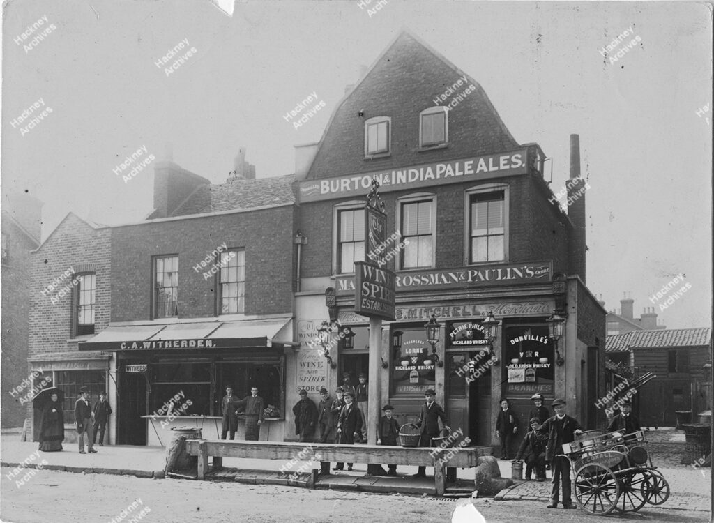 Lower Clapton Road, west side. Includes The Windsor Castle public house, C. A. Witherden, Parts Tailor and T. Coxall on tricycle/hand cart. Men woman and children in Victorian dress, c.1880