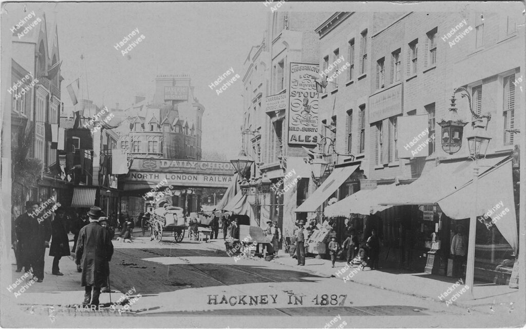 Mare Street, Hackney during Golden Jubilee. 1887.  looking north to railway bridge from corner of Graham Road during Queen Victoria’s Golden Jubilee celebrations. Includes King’s Head public house. The Railway bridge has the words north London Railway printed on it.