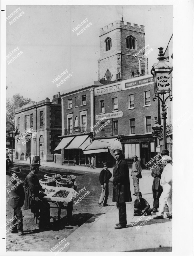 Mare Street looking north from railway bridge. Includes Hackney Tower and Old Town Hall and shell fish barrow, c.1890