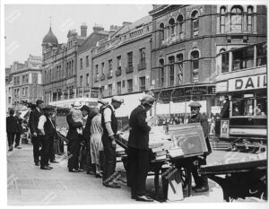 Bookstalls and sellers on Shoreditch High Street looking north east. Includes Jeremiah Rotherham's factory, Brandons Progressive Tailors, c.1930.