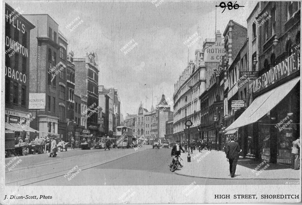 Shoreditch High Street. Includes market stalls, shops, buses, cars, vans and a man on a motorbike. 1932.
