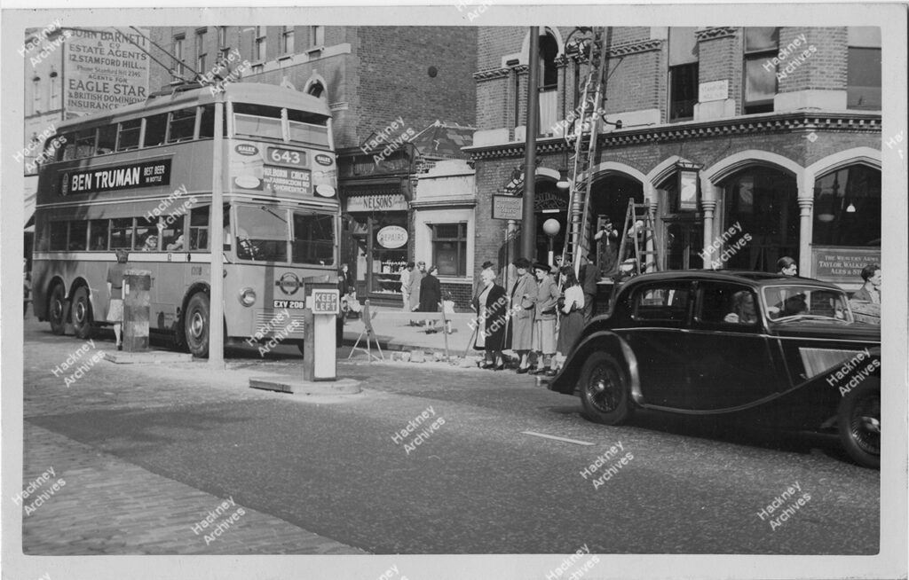 Pedestrians crossing outside The Weavers’ public house as part of Borough Road safety survey, 2-12 Stamford Hill. Includes trolley bus, c.1950.