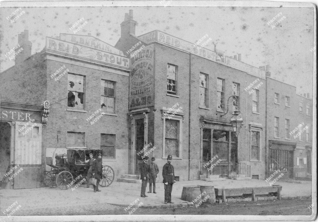 The White Hart Hotel, Lower Clapton Road after a possible gas mains burst. A police man in uniform stand at the side of the road and a horse drawn carriage is in the background., c.1900.