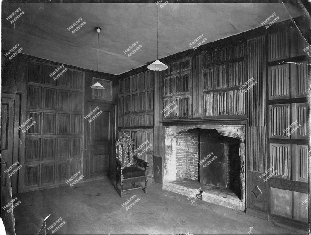 Interior of Sutton House, Homerton High Street, Homerton Hackney, c.1905. The Cromwell panelled room and fireplace at Sutton House (St John’s Church Institute). Includes electric bulbs and lamps.