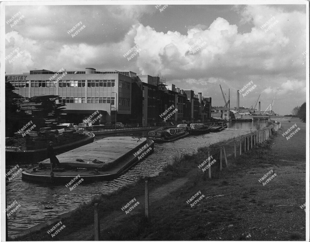 The Lesney Matchbox Factory, Lee Conservancy Road, Hackney. View from the east side of River Lea Navigation. Includes barges on the river and loading cranes in the background, 1966.