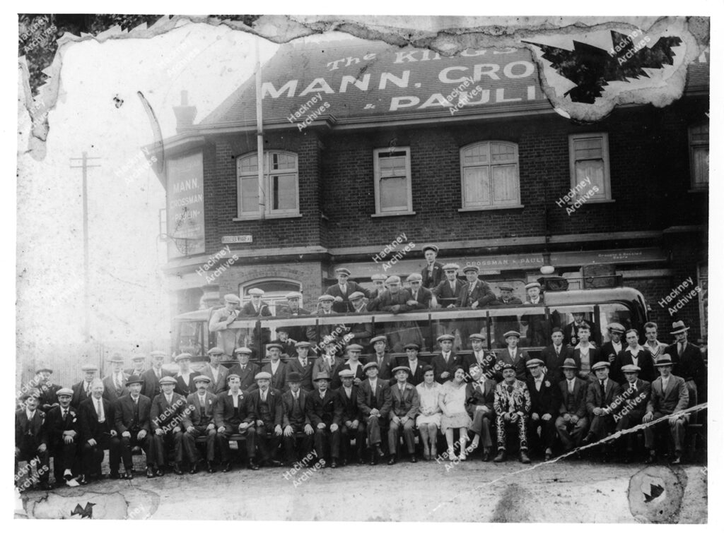 Group photo outside The Kings Head public house,  Group of men and women are sat in front of motor vehicle, charabanc.Middlesex Wharf, Hackney, c.1929.