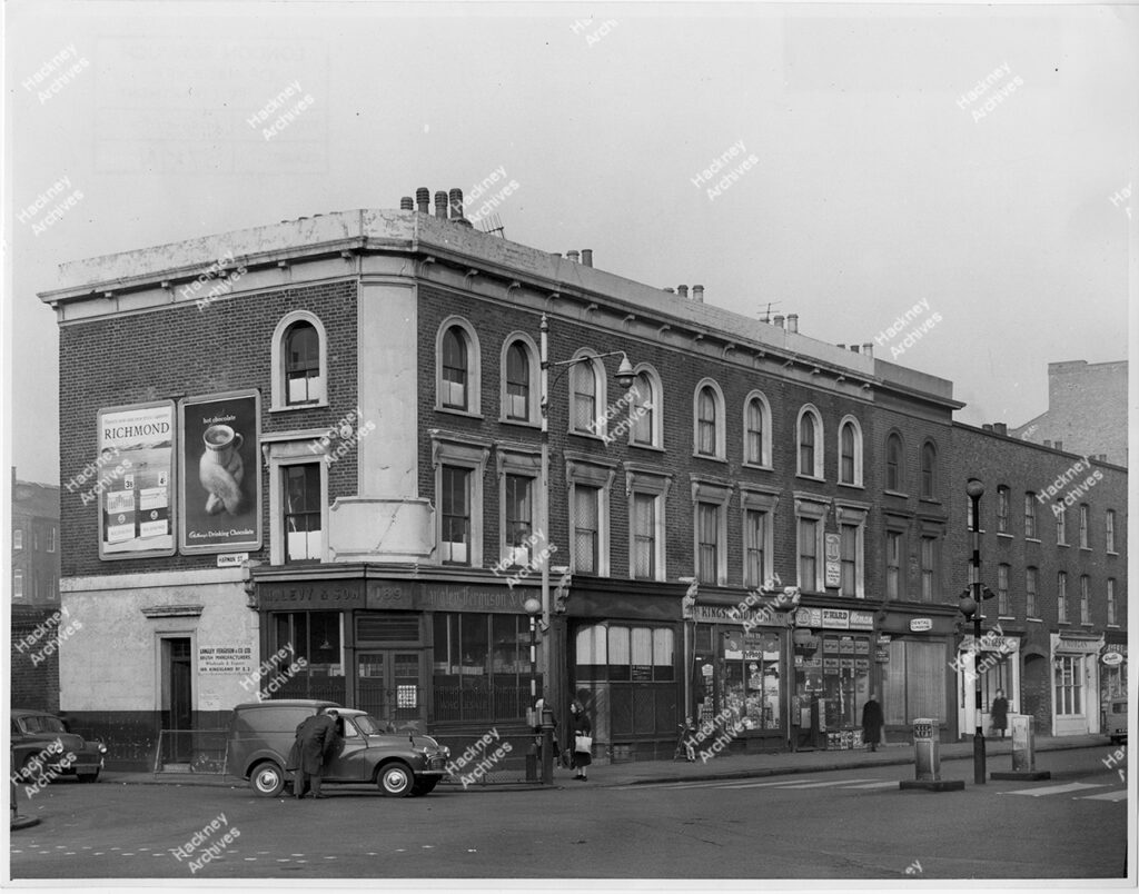 Corner of 189-199 Kingsland road and Harman Street (Hare Walk). Includes Langley Ferguson & Co. LTD, Kingsland Dairy, T. Ward, Dental Surgeon, Henry Gess, F. Morgan shops. Vans and cars. 1964.