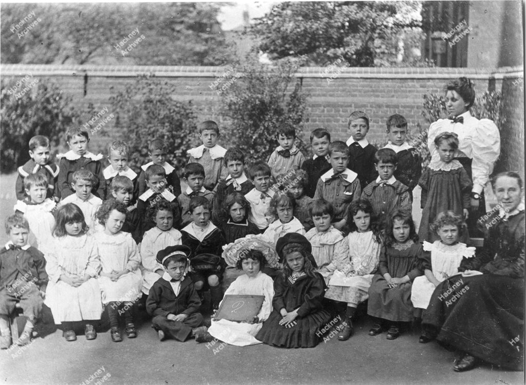 School group photo of young children and teachers at Chatham Palace Board School, Chatham Place, Hackney. Includes Marshall, Marshall, Miss Walker, Arthur Walker, Rose Cousins, Hargreaves, Hill Pomeray, Daisy Hill, Miss Evans, Gordon Patrick, Maud Patrick. 1899.